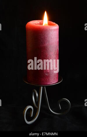 Une bougie rouge dans un support noir sur fond noir Banque D'Images