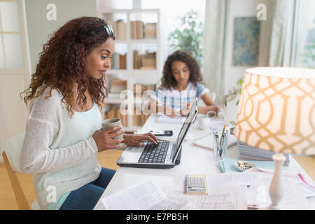 Woman using laptop at home, girl (8-9) à faire leurs devoirs en arrière-plan Banque D'Images