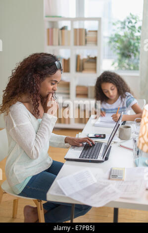 Woman using laptop at home, girl (8-9) à faire leurs devoirs en arrière-plan Banque D'Images