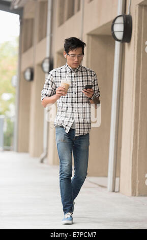 Homme marchant sur un trottoir avec un café glacé et d'un téléphone mobile Banque D'Images