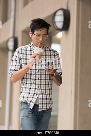 Homme marchant sur un trottoir avec un café glacé et d'un téléphone mobile Banque D'Images