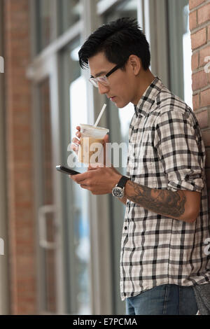 Homme marchant sur un trottoir avec un café glacé et d'un téléphone mobile Banque D'Images