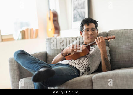 Homme assis sur un canapé et jouer ukulele Banque D'Images