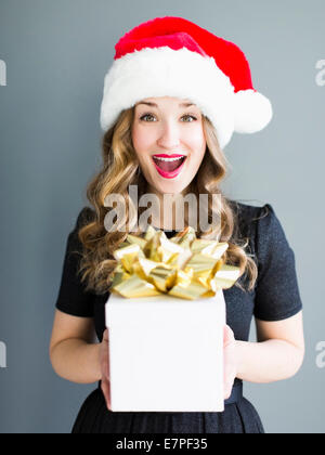 Studio portrait of woman wearing Santa hat holding gift Banque D'Images