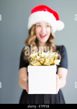 Studio portrait of woman wearing Santa hat holding gift Banque D'Images