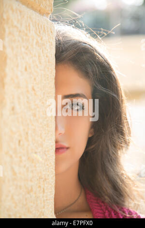 Jeune femme se cachant derrière un mur Banque D'Images