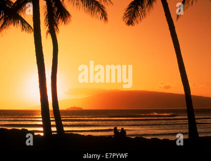 Couple sous les palmiers sur l'île de Maui au coucher du soleil avec l'île de Lanai sur horizon Banque D'Images