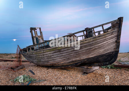 Un vieux bateau de pêche en bois naufragé sur une plage de galets sous la lumière de la pleine lune Banque D'Images