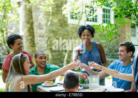 Une réunion de famille, hommes femmes et enfants autour d'une table dans un jardin en été. Banque D'Images