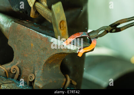 Faire de l'élément décoratif dans la forge sur l'enclume. Marteler en acier brillant. Forgeron forge un fer à cheval. Banque D'Images