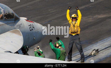 Un marin de l'US Navy sur l'équipage dirige un F/A-18F Super Hornet pendant les opérations de vol du porte-avions USS George H. W. Septembre 22, 2014 Bush dans le golfe Persique, le 22 septembre 2014. L'armée a lancé la première frappe directe sur les cibles d'ISIS à l'intérieur de la Syrie. Banque D'Images