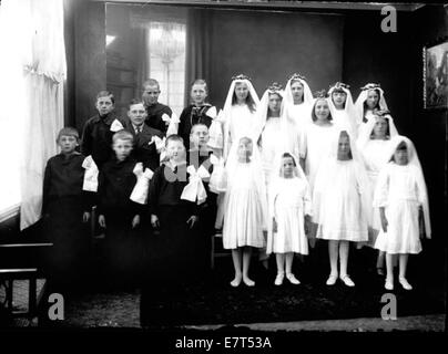 Il s'agit d'un portrait de groupe du début du XXe siècle, pris entre 1910 et 1929, montrant des enfants en tenue religieuse. Certaines filles portent des robes blanches et des voiles, et les garçons sont habillés dans des vêtements formels. La photographie reflète une cérémonie religieuse, probablement une confirmation ou un événement similaire. Banque D'Images