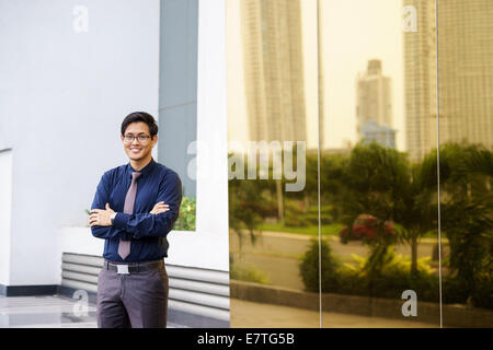 Portrait of Chinese businessman standing with arms crossed près de l'immeuble de bureaux à Panama. Réflexions de miroir sur la ville Banque D'Images