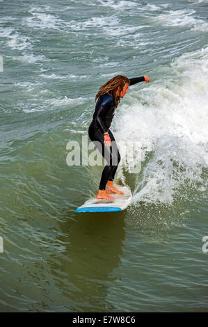 Surfer avec des dreadlocks en noir bottines équitation sur des vagues de surf comme il casse le long de la côte de la mer du Nord Banque D'Images