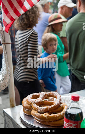 New York, New York - un garçon regarde rêveusement à bretzels en vente sur un vendeur de rue's panier que sa mère se déplace le long de lui. Banque D'Images