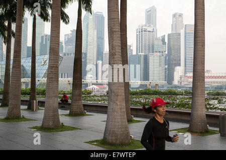 Une femme reprend sa course sur le bord de l'eau avec le quartier central des affaires dans l'arrière-plan, à Singapour Banque D'Images