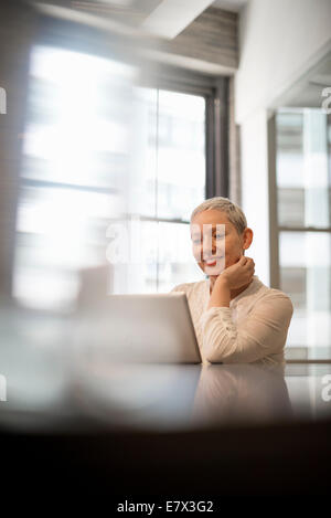 La vie de bureau. Une femme assise à l'aide d'un ordinateur portable. Banque D'Images