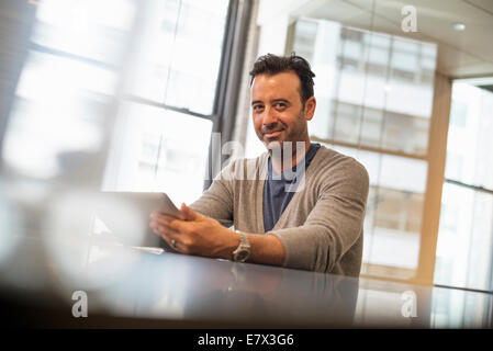 La vie de bureau. Un homme assis à un bureau à l'aide d'une tablette numérique. Banque D'Images