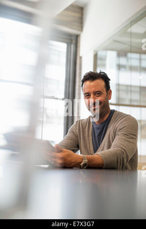 La vie de bureau. Un homme assis à un bureau à l'aide d'une tablette numérique. Banque D'Images