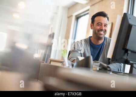 La vie de bureau. Un homme assis à un bureau à l'aide d'un ordinateur. Banque D'Images