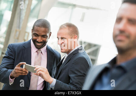 Deux hommes d'contrôler un téléphone et rire, un homme à l'avant. Banque D'Images