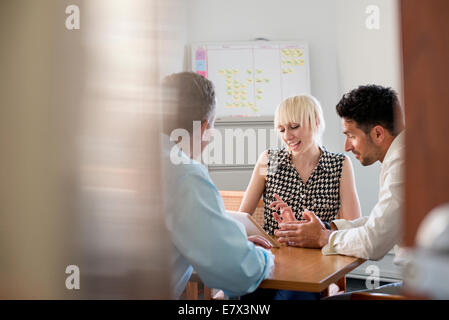 Trois collègues d'affaires dans un bureau à parler autour d'une table et à la tablette numérique à un. Banque D'Images