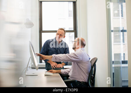 Deux collègues dans un bureau de parler et se référant à l'écran d'un ordinateur. Banque D'Images