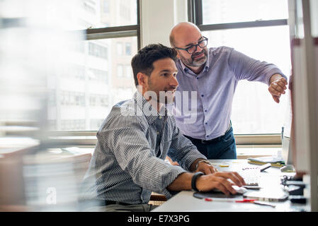 La vie de bureau. Deux hommes dans un bureau, à l'aide d'un écran d'ordinateur. Banque D'Images