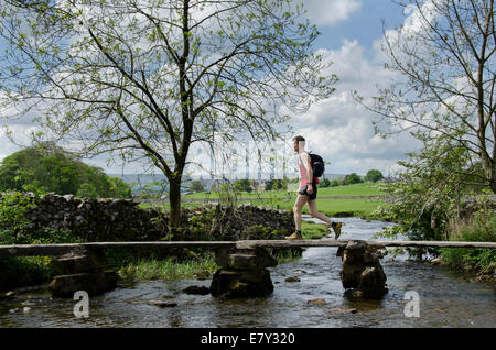 L'homme en jogging de sport en pierre historique passage clapper pont sur Austwick Beck dans le magnifique paysage de la campagne, - du Yorkshire, England, UK. Banque D'Images
