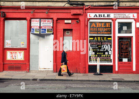 Homme marchant passé une école de conduite automobile et des petites entreprises un barricadèrent shop à Leith, Édimbourg Banque D'Images