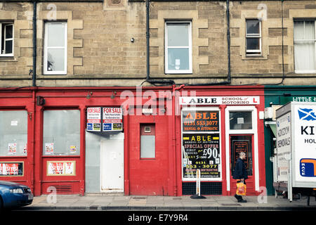 Homme marchant passé une école de conduite automobile et des petites entreprises un barricadèrent shop à Leith, Édimbourg Banque D'Images