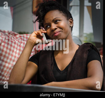 Jeune femme assise au café noir talking on phone Banque D'Images