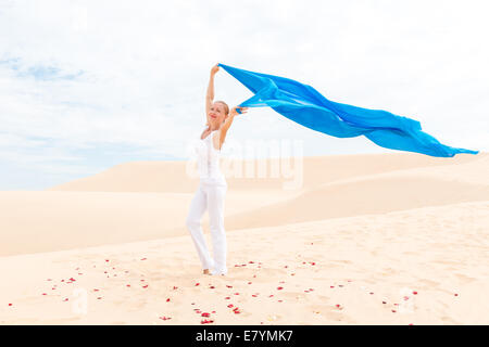 Young woman wearing white slim avec flying blue scarf in desert Banque D'Images