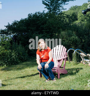 Femme assise sur le bord de la chaise en bois sur la pelouse Banque D'Images