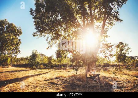 Young woman playing guitar under tree Banque D'Images