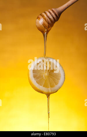 Le miel s'écoule sur tranche de citron, studio shot sur fond jaune Banque D'Images