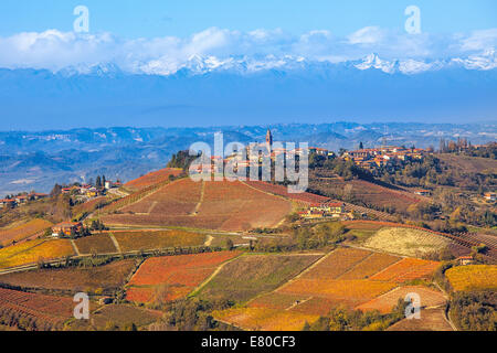 Petite ville sur la colline avec des vignes d'automne et les montagnes en arrière-plan dans le Piémont, Italie du Nord. Banque D'Images