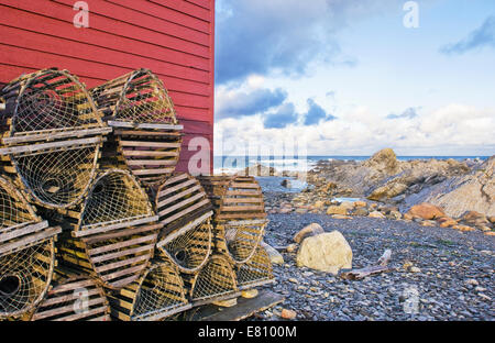 Casiers à homard empilés contre un abri de pêche rouge à Terre-Neuve, Canada Banque D'Images
