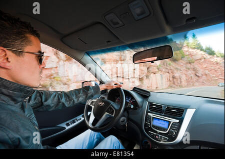 Portrait horizontal d'un jeune homme marocain au volant d'une voiture à conduite à gauche dans le Haut Atlas au Maroc. Banque D'Images