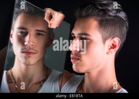 Beau jeune homme narcissique d'admirer son reflet dans le miroir sur un salon de l'auto-absorption Banque D'Images