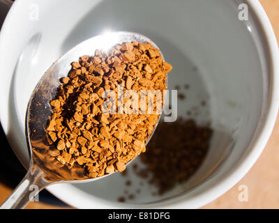 Le café instantané granules sur une cuillère à café, est versé dans une tasse. Banque D'Images