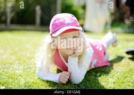 Petite fille de cinq ans posant dans le jardin à la recherche et smiling at the camera Banque D'Images