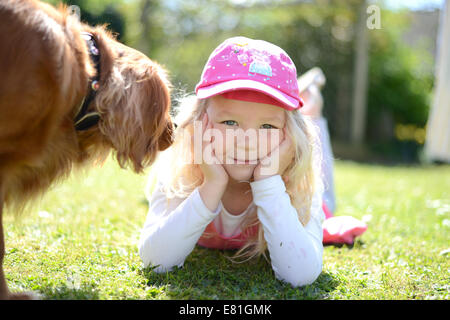 Petite fille de cinq ans posant dans le jardin souriant à l'appareil photo avec un chien en marche sur prise Banque D'Images