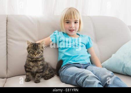 Petite fille assise sur le canapé en caressant son chat Banque D'Images