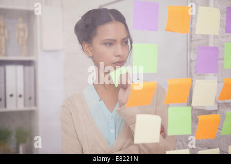 Thoughtful businesswoman looking at sticky notes sur la fenêtre Banque D'Images