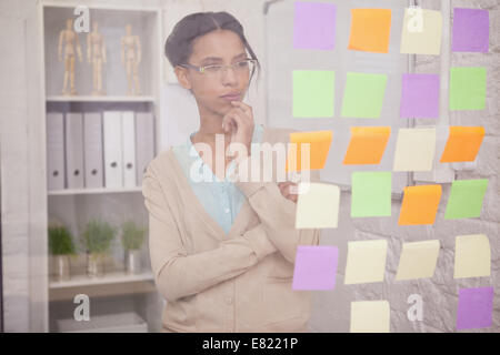 Thoughtful businesswoman looking at sticky notes sur la fenêtre Banque D'Images