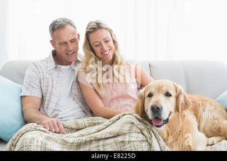 Affectionate couple sitting on sofa sous couverture avec leur chien Banque D'Images