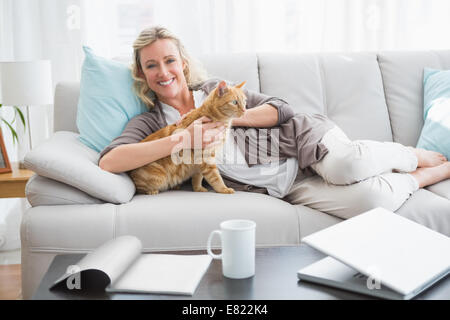 Cheerful woman lying on sofa de câliner un chat de gingembre Banque D'Images