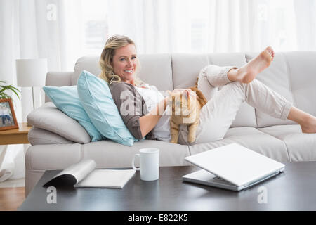 Cheerful woman lying on sofa de câliner un chat de gingembre Banque D'Images