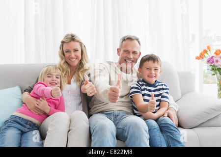 Happy Family sitting on sofa giving Thumbs up Banque D'Images